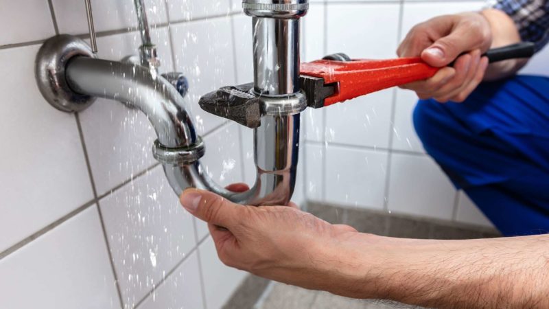 Plumber using wrench on a leaking pipe