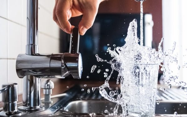 Water faucet splashing water into a glass