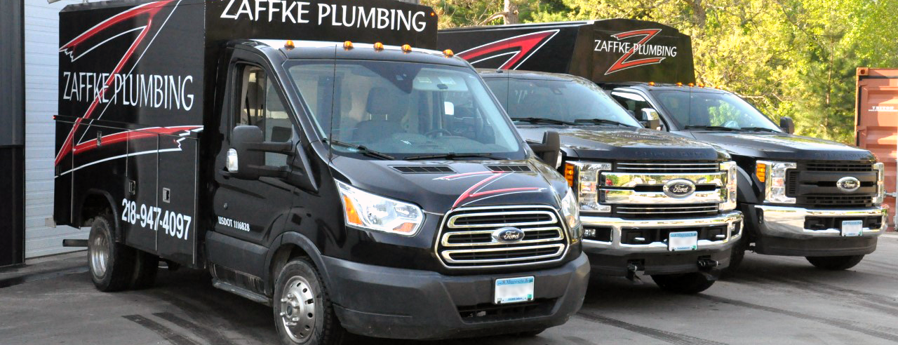 Zaffke Plumbing branded trucks in front of an equipment barn